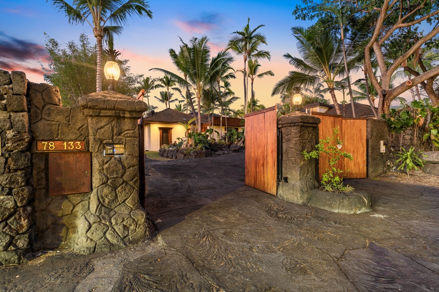 Stone entrance gate with tropical palms and warm sunset lighting creates a welcoming arrival experience.