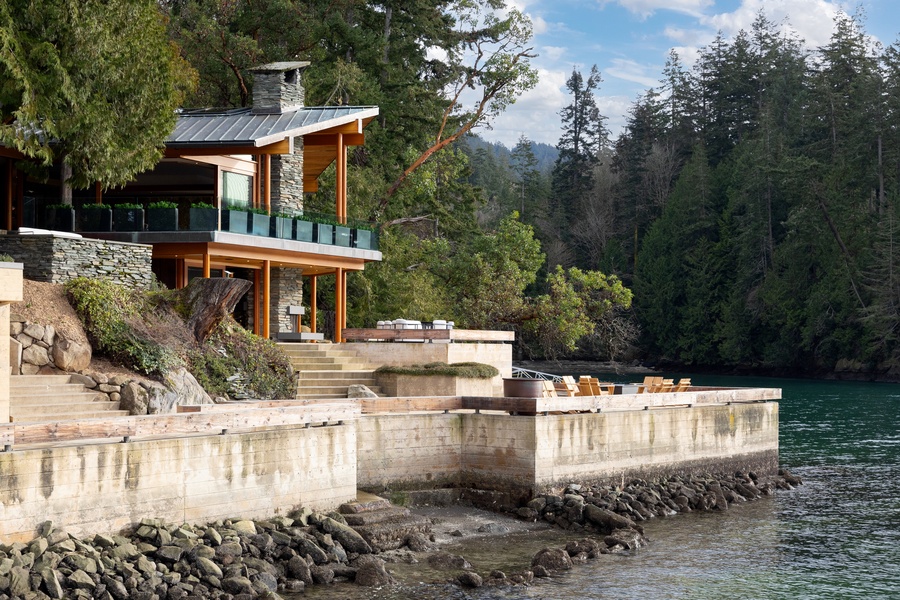 Modern lakefront property featuring contemporary architecture nestled among towering evergreens with private waterfront access and mountain views.