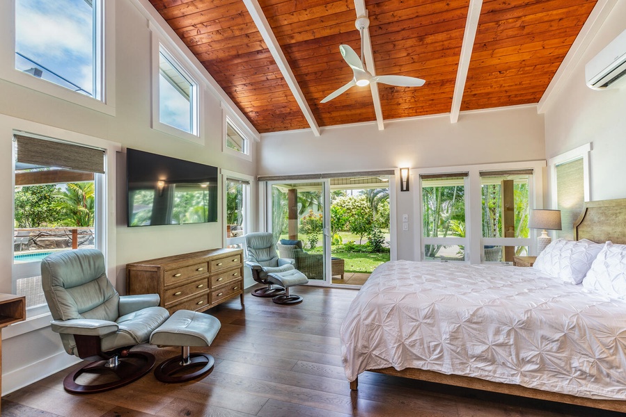 Relax in the bright primary suite at Lani Oasis, where large windows bring the lush tropical surroundings indoors.