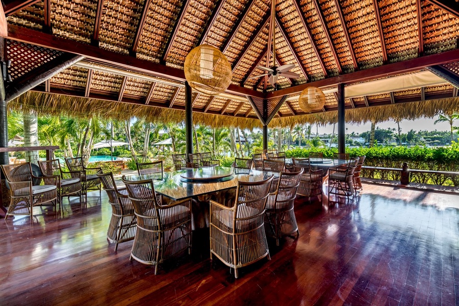 Expansive thatched-roof pavilion with glass-top tables and wicker chairs.