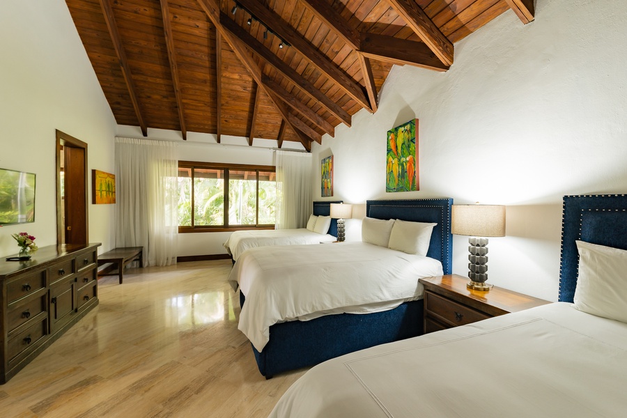 Spacious guest bedroom with vaulted ceiling, three beds, and vibrant artwork.