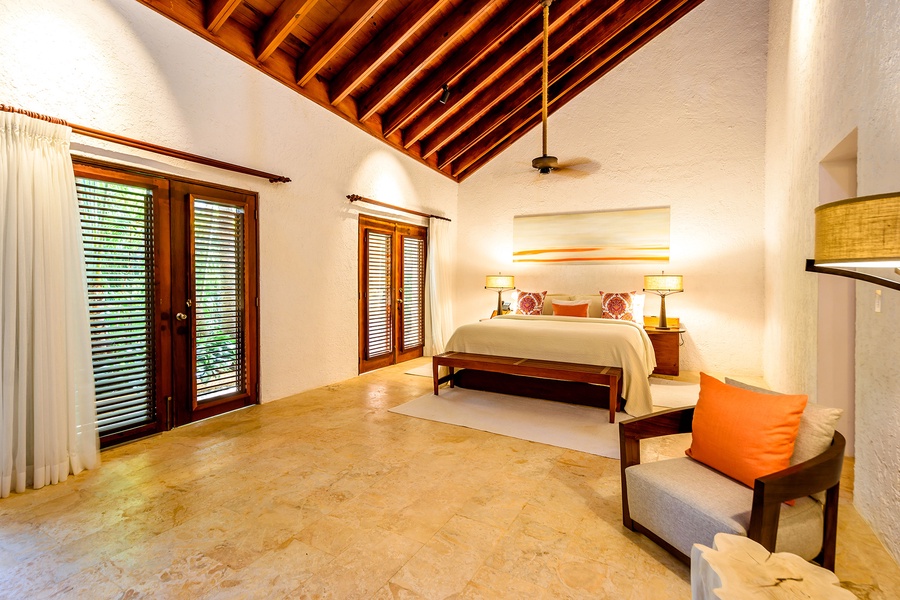 Cozy guest bedroom with seating area and high ceiling.