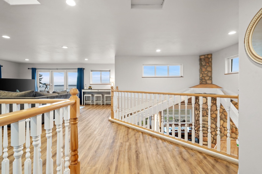 Your upstairs loft offers bright, airy space with wood railings and ocean glimpses through multiple windows.