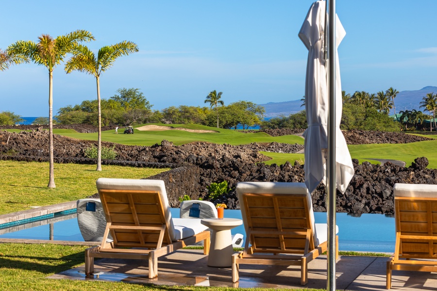 Luxury poolside loungers overlook ocean views and championship golf greens surrounded by tropical palms and volcanic rock formations.
