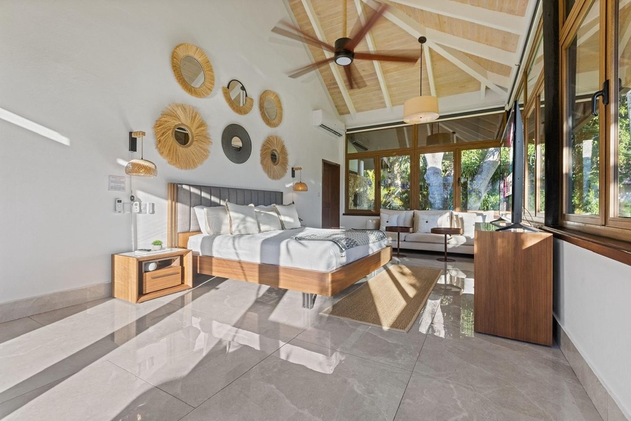 The primary bedroom features a large windows offering a view of the lush greenery outside.