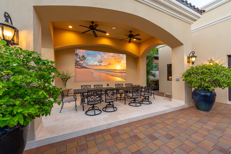 Covered outdoor dining area with ceiling fans, cozy seating, and a vibrant sunset view.