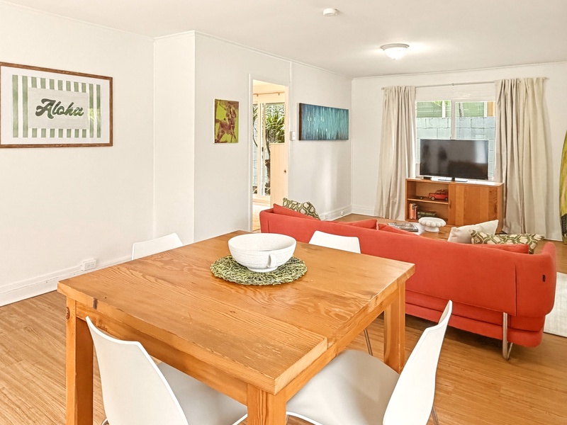 Gather around this warm wooden dining table while your vibrant coral sofa beckons for post-meal relaxation in your bright, cheerful home.