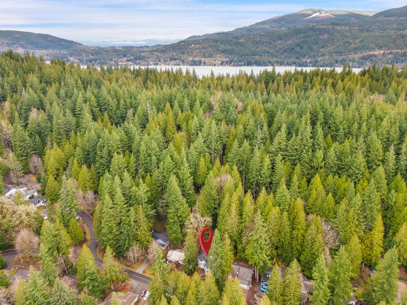 Aerial view of property nestled in pristine Pacific Northwest forest with lake and mountain backdrop creating a peaceful retreat setting.