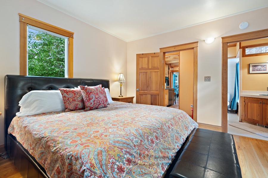 Unwind in your serene bedroom with rich wood details, cozy paisley bedding, and peaceful garden views.