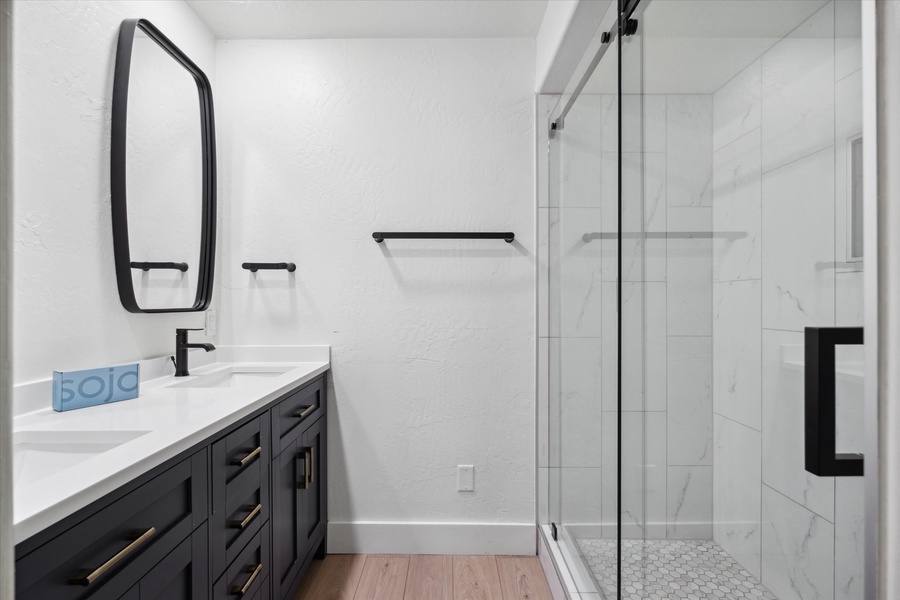 Common bathroom with dual sink and a huge walk-in shower on a glass enclosure.
