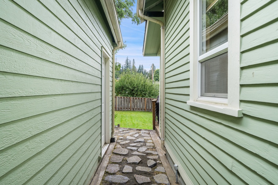 A charming pathway framed by the home’s exterior leads to the peaceful backyard, inviting you to explore and unwind.