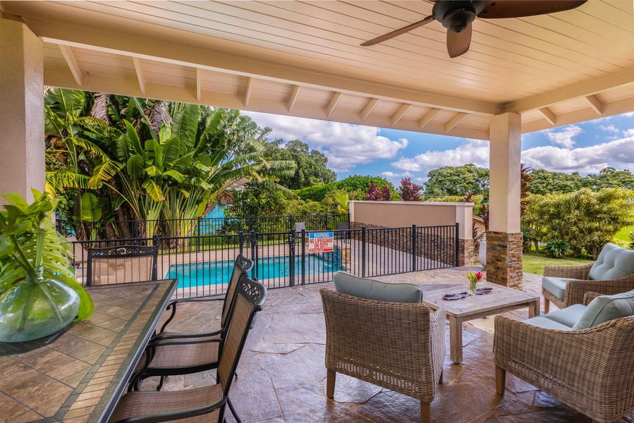 Poolside seating area at Pohaku Villa, offering a relaxing spot beside lush landscaping.