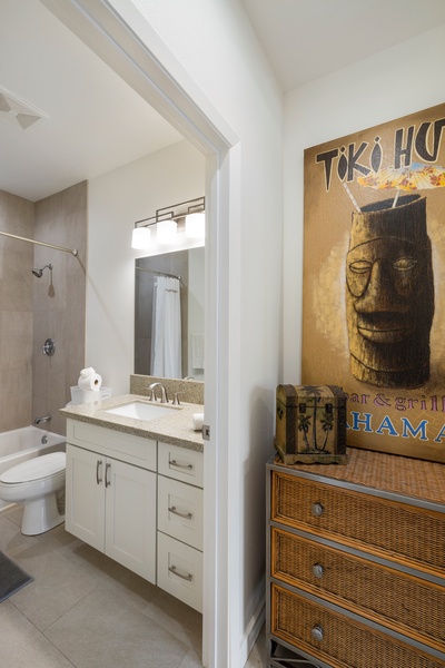 Ground-floor guest bathroom with full-size tub, tropical artwork, and spacious vanity.