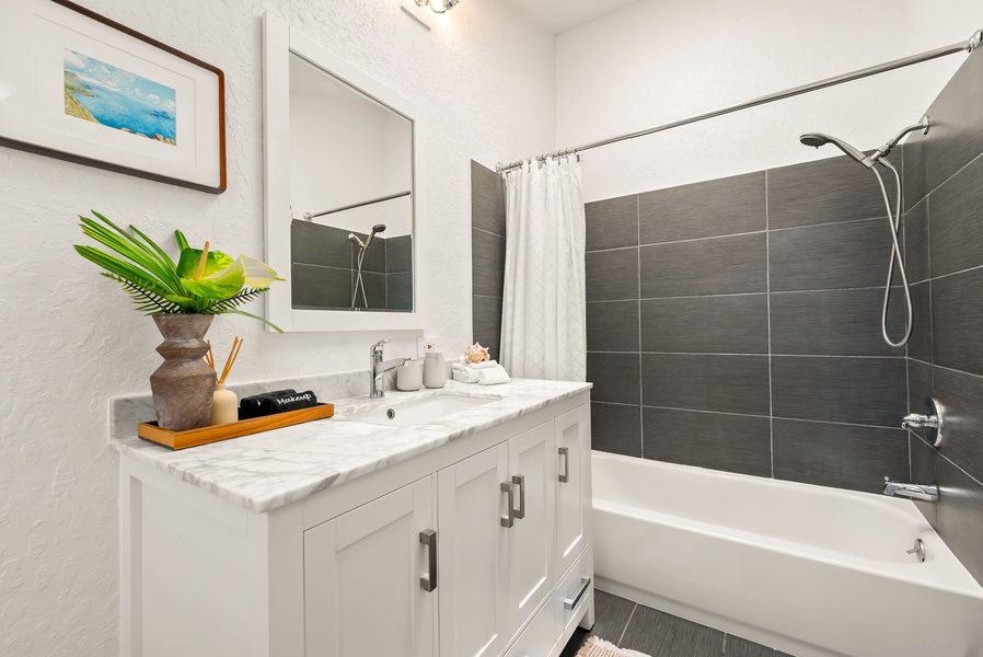 Step into your private oasis with sleek gray tiling, a marble-topped vanity with fresh greenery, and a relaxing tub-shower combo awaiting your arrival.