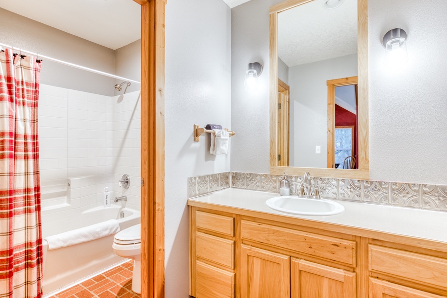 The shared guest bathroom with a shower/tub combo and a vanity for storage.
