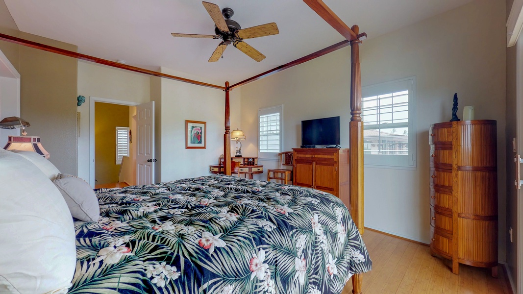 The upstairs primary guest bedroom features a TV, dresser an ceiling fan.