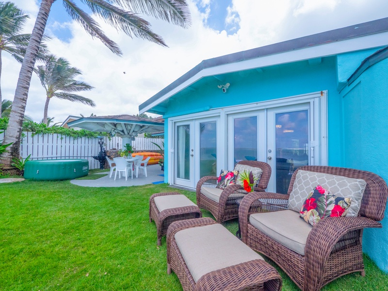 Relax in your private tropical oasis with wicker seating on lush lawn, swaying palms overhead, and bright island-style architecture creating the perfect Hawaiian getaway.