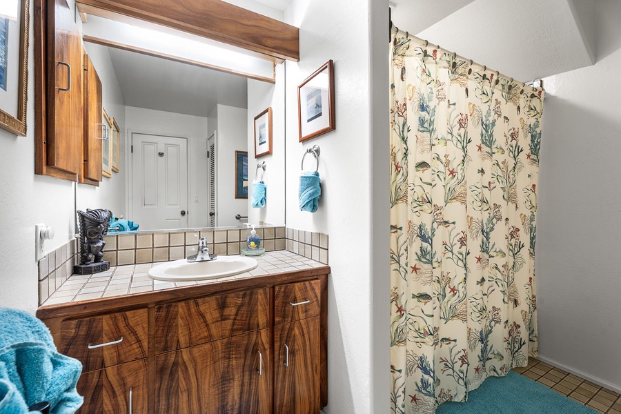 Your charming bathroom features warm wood vanity, botanical shower curtain, and thoughtful turquoise accents creating a cozy, home-like retreat.