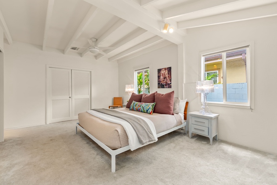 Your serene bedroom retreat features vaulted ceilings, soft natural light streaming through windows, and a plush bed dressed in layers of comfort—perfect for unwinding after sunny days exploring.