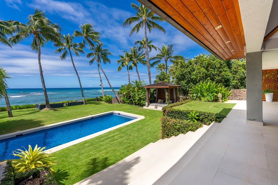 A beachfront tropical paradise featuring a sleek pool, lush green lawns, swaying palms, and serene ocean views—perfect for an unforgettable Hawaiian getaway.