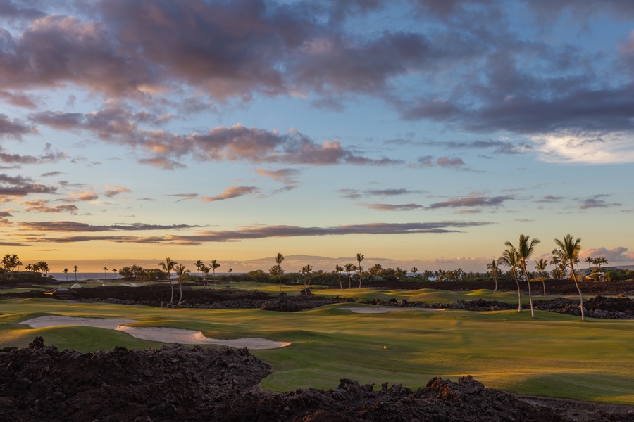 This serene golf course view captures the essence of a tranquil evening, with lush fairways framed by volcanic rock under a spectacular sunset sky.