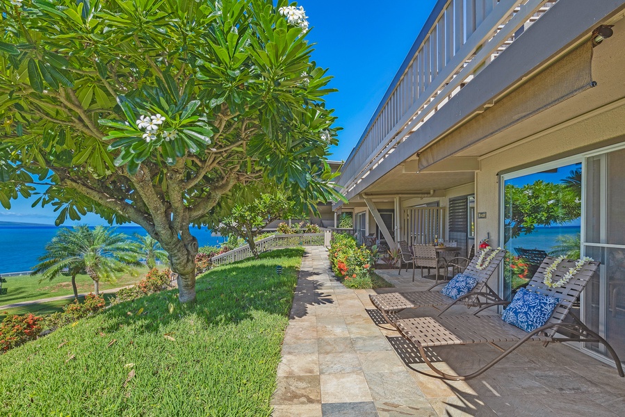 Enjoy a peaceful moment on the shaded lanai, surrounded by lush greenery and ocean views, perfect for relaxing in the fresh air.