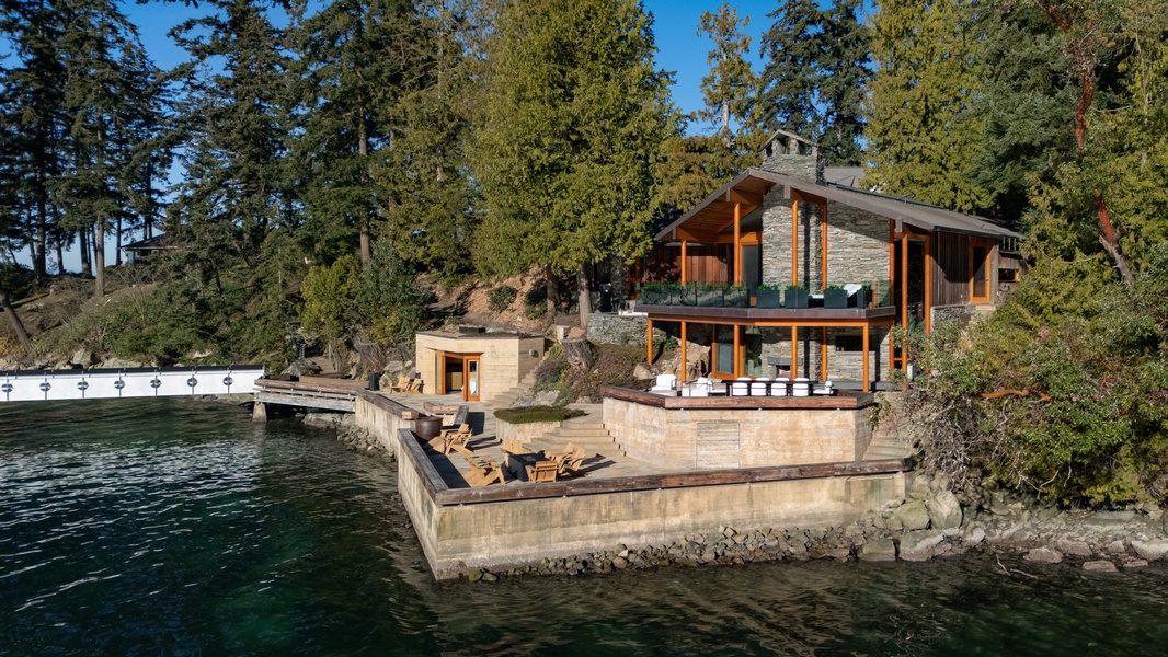 Modern waterfront retreat nestled among towering evergreens with private dock and terraced outdoor spaces overlooking pristine waters.