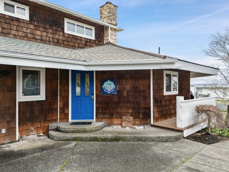 Charming coastal cottage with rustic cedar shingles, stone chimney, and welcoming blue front door creating an authentic seaside retreat experience.
