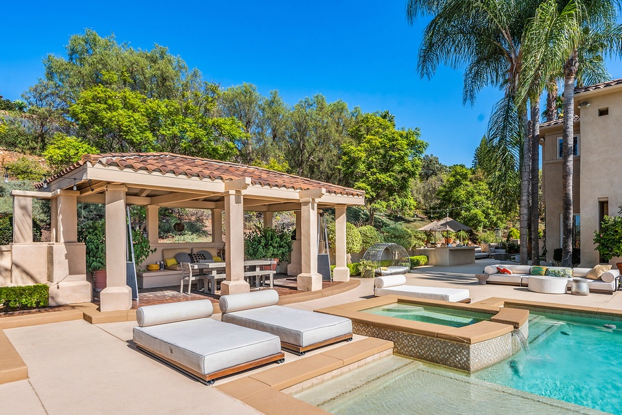 A covered outdoor living/dining room, summer kitchen with bar seating, raised bed gardens, all surrounded by beautiful mature palms and landscape.