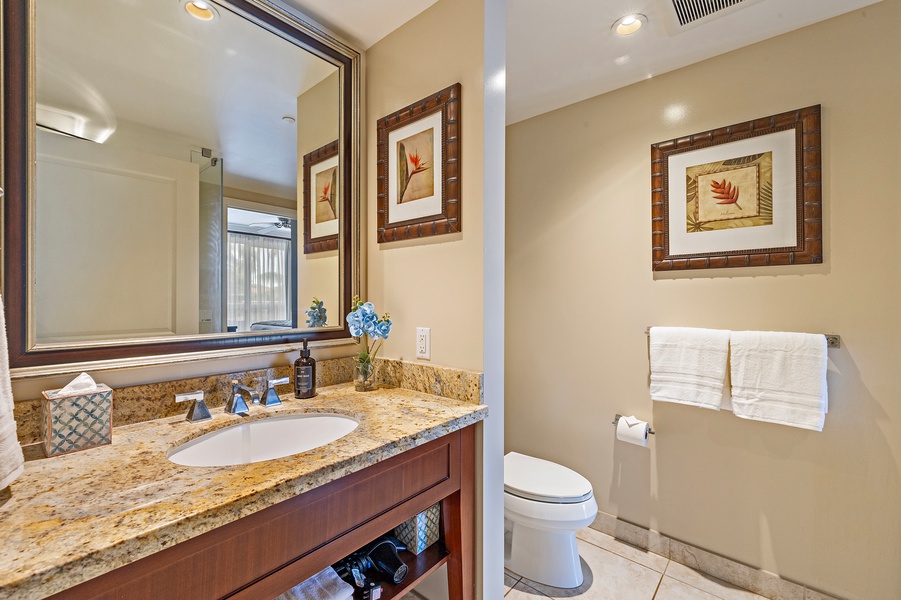 The ensuite bathroom featuring a spacious vanity with rich wood tones and a granite countertop.