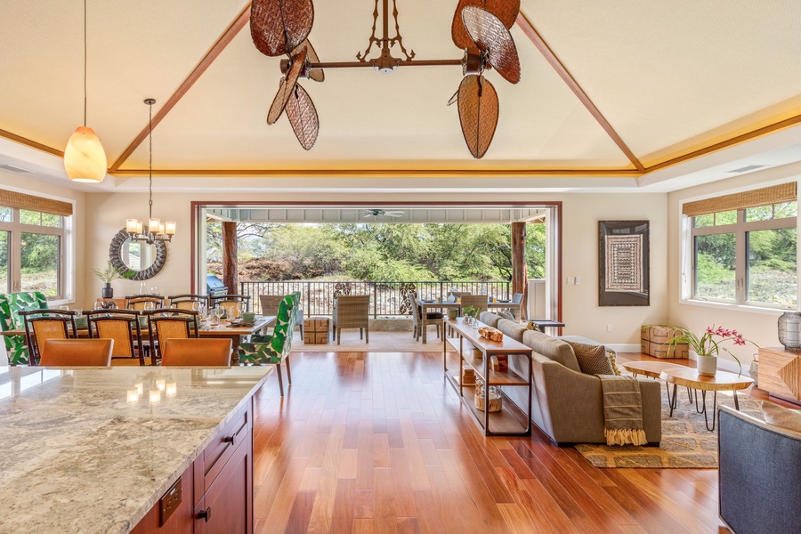 Wide view of great room, featuring dining table (left), living area (right), and upstairs terrace with sliding glass pocket doors.