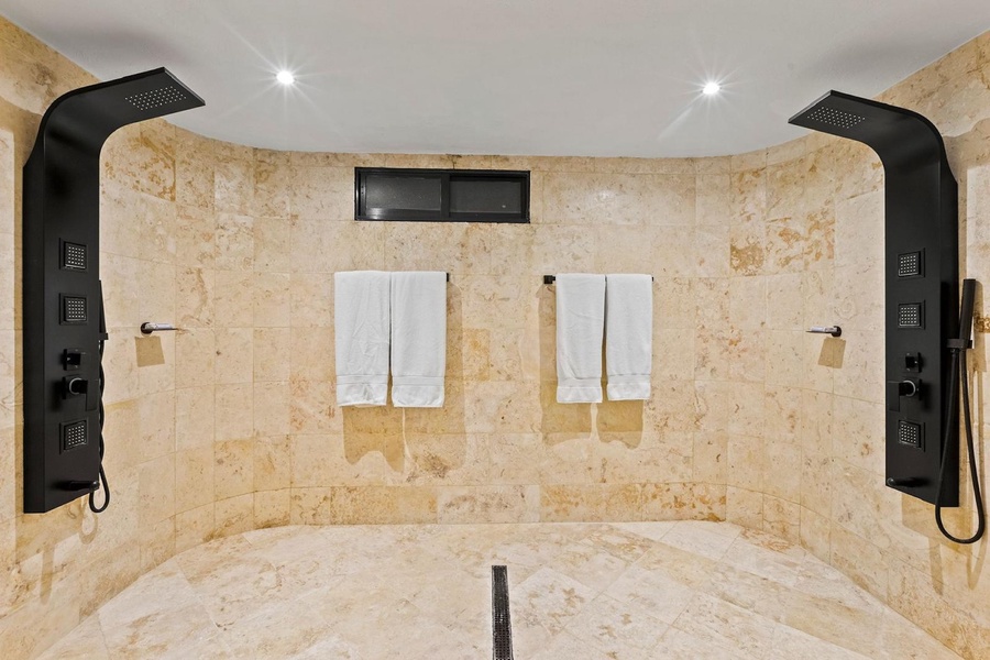 A luxurious shower room featuring dual rainfall shower heads and smooth stone tiles.