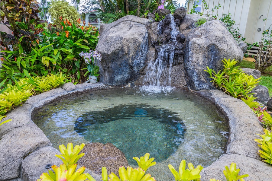 A beautiful pond with a gentle waterfall surrounded by flowers.