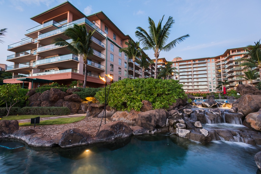 The resort's tropical landscaping and soft lighting provide a peaceful atmosphere at dusk, with tiki torches illuminating the pathway.