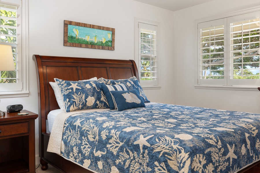 Drift off in your coastal-themed bedroom featuring ocean-blue linens and warm wood furnishings, with natural light streaming through plantation shutters.