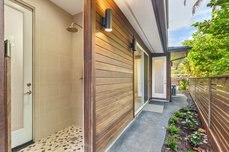 Side entrance with a private outdoor shower and lush garden surroundings.