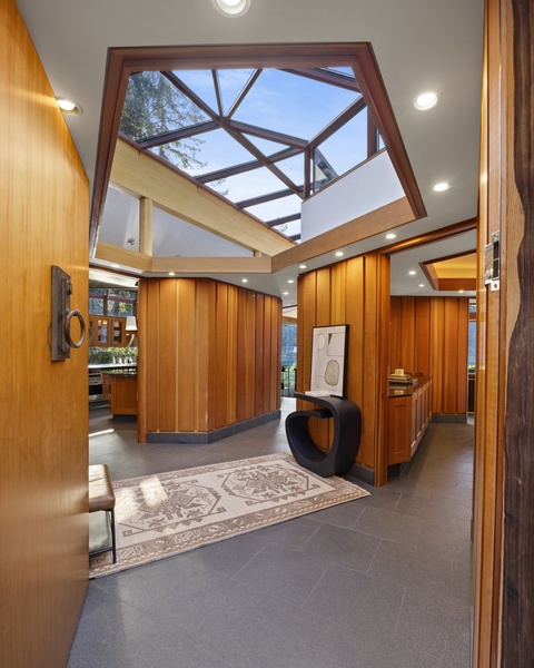 Step into this stunning wood-paneled foyer where natural light streams through the glass ceiling above, creating warmth throughout the space.