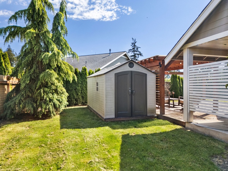 Backyard area with covered patio, garden shed, and mature landscaping provides private outdoor space for relaxation and storage during your visit.
