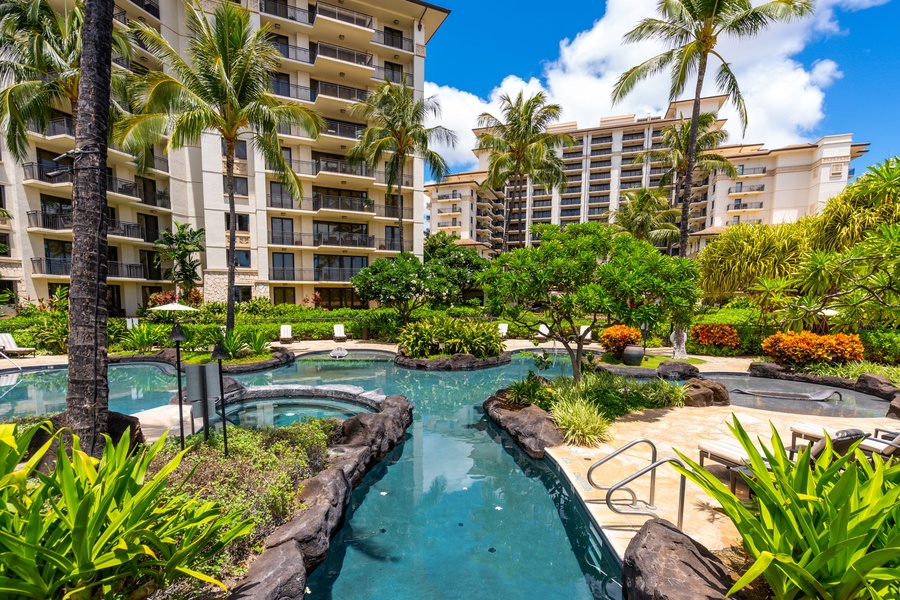Resort-style tropical pool area surrounded by lush landscaping and towering palm trees beneath multiple high-rise buildings.