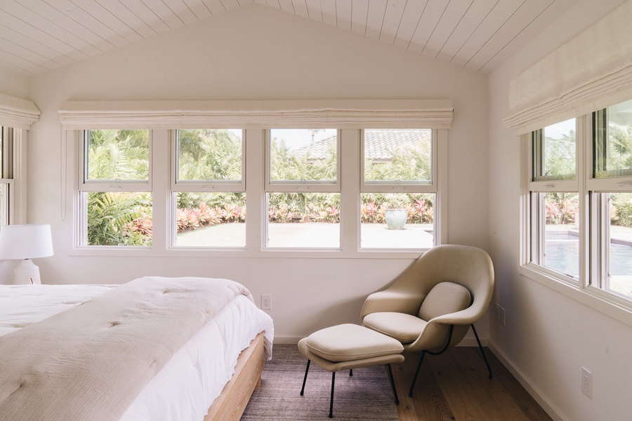A bright and inviting bedroom with a cozy reading chair and garden-facing windows.