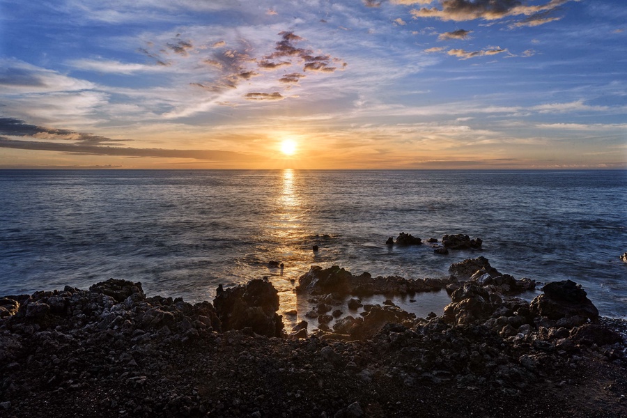 Golden sunset paints the sky above rocky coastline and endless ocean waters.