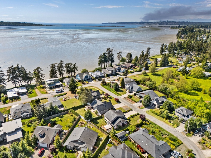 Aerial view of a tranquil beachfront neighborhood with tidal flats and coastal waters, surrounded by lush greenery and offering serene waterfront access.
