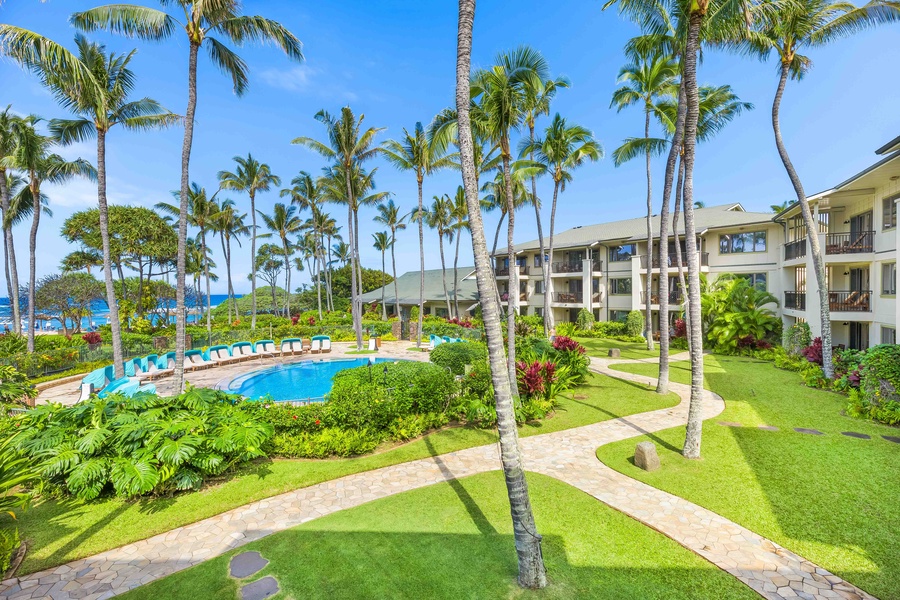 Tropical paradise resort with palm-fringed pool, oceanfront buildings, and lush landscaped gardens under brilliant blue skies.