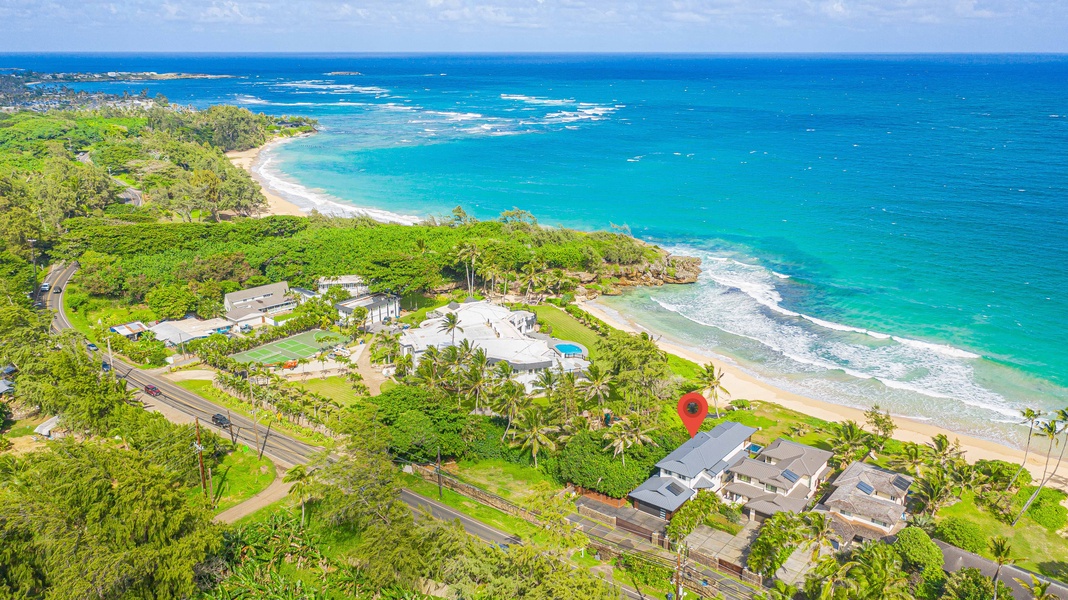 Panoramic aerial shot capturing the lush coastal surroundings and nearby beach access.