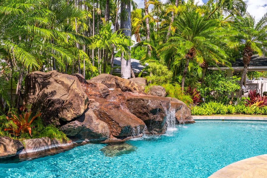 Inviting pool with a natural rock waterfall feature, surrounded by lush greenery for a tropical retreat.