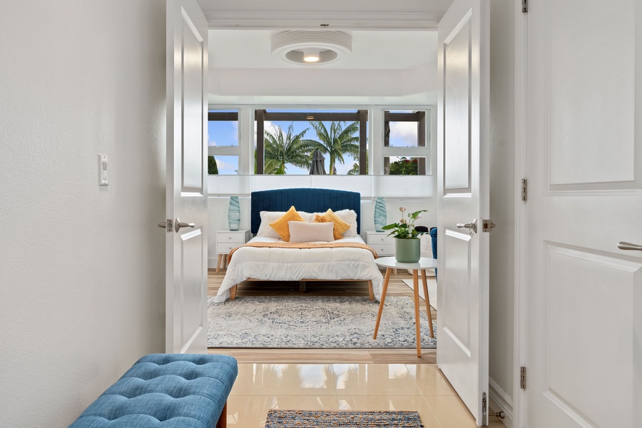 Step into the serene Primary Suite with gleaming hardwood floors leading towards a cozy bed, framed by a stylish blue headboard.