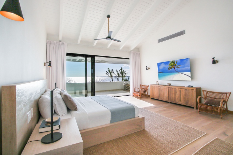 Wake up to ocean views in this primary bedroom with a large TV and access to a private balcony.