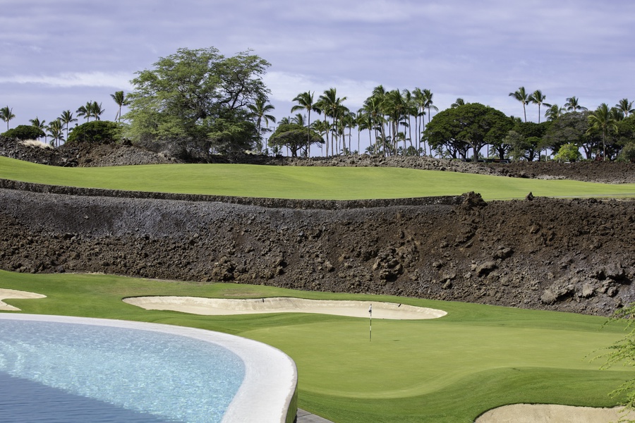 Championship golf course featuring pristine greens, strategic bunkers, and tropical landscaping with palm trees and volcanic rock walls.