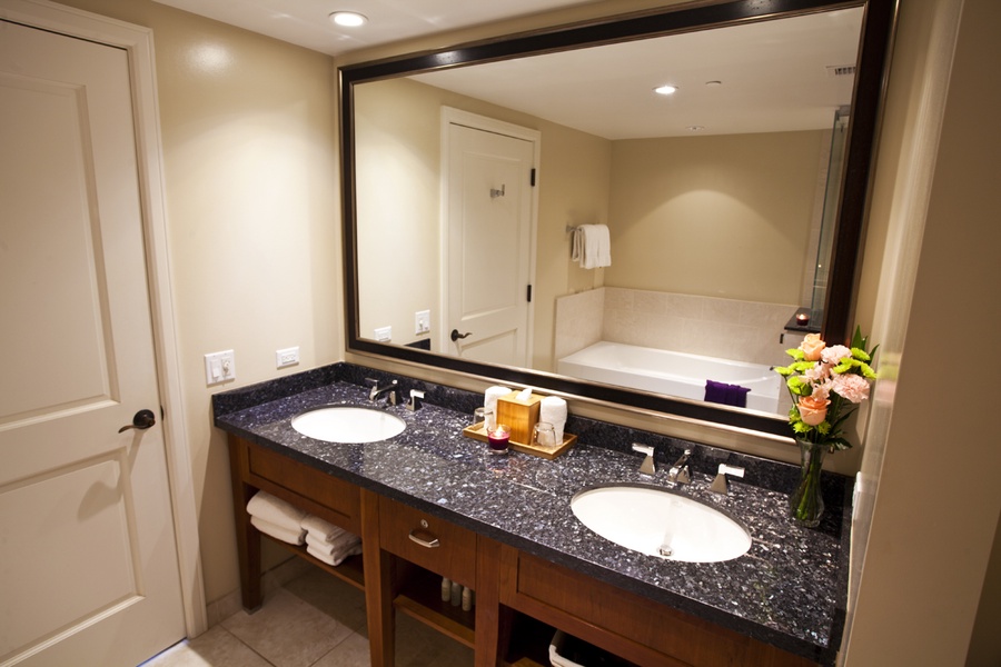 The spacious bathroom offers dual sinks with a sleek granite countertop and the deep soaking tub in the background provides a perfect spot for relaxation after a day of exploring the island.