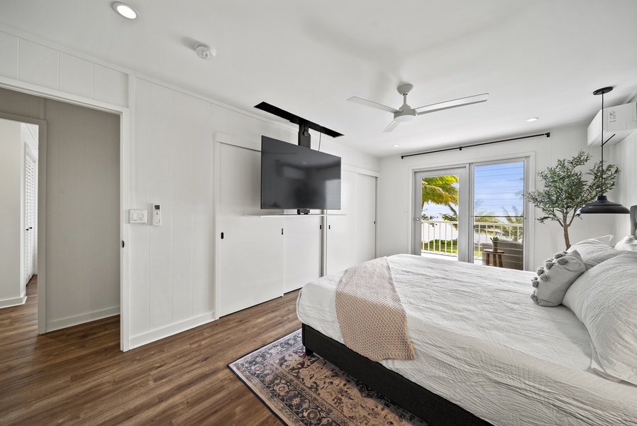 Primary suite with a king-sized bed, ceiling-mounted TV, and lanai access, offering luxurious relaxation after beachfront adventures.